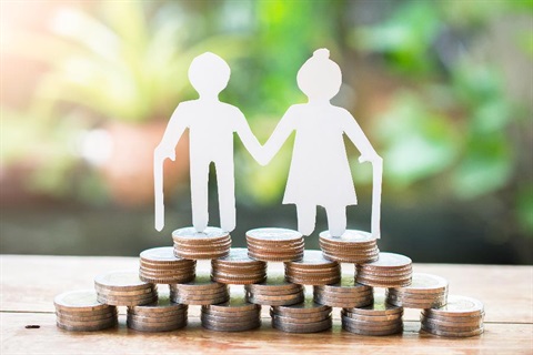 White paper cut-out of an elderly couple standing on a pile of coins.