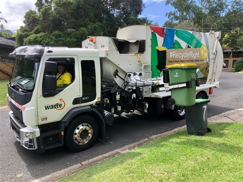 A council garbage truck collecting a yellow recycling bin from the kerb.