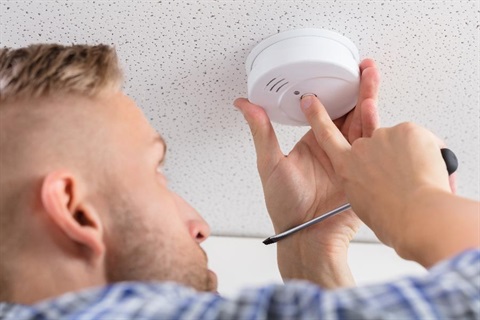 A man installs a smoke alarm on the ceiling.