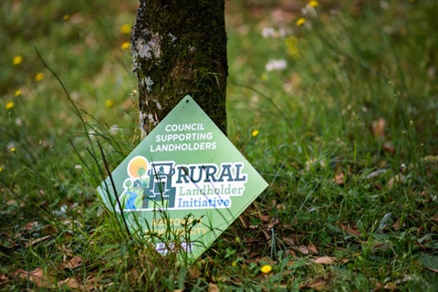 The Rural Landholder Initiative sign resting against a tree trunk.