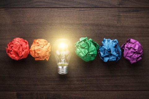 A line of scrunched up paper balls, in each colour of the rainbow, with one replaced by a light bulb.