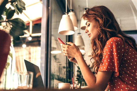A woman sits in a cafe looking at her smartphone.