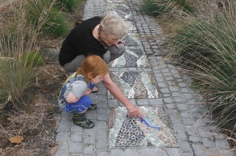 A woman showing a mosaic path to a little girl.
