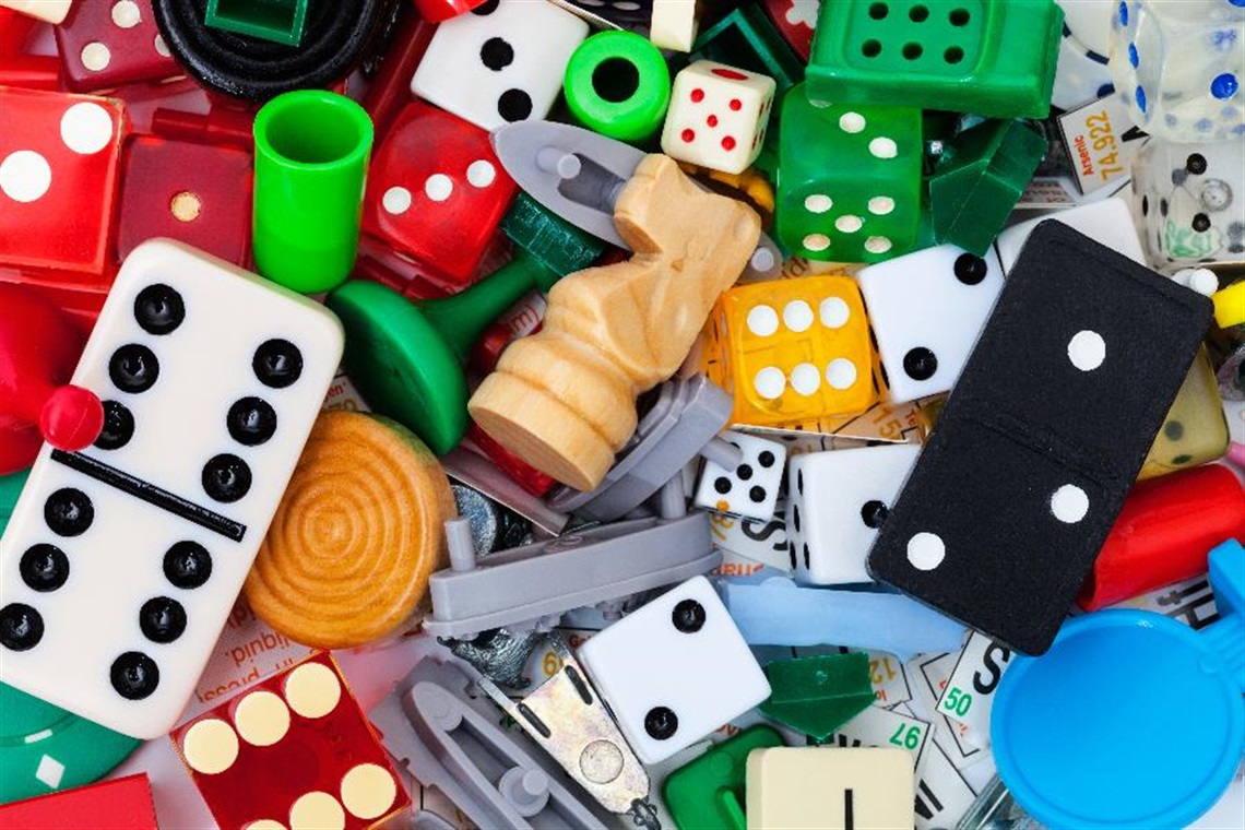 A close-up of a pile of dominoes, dice and board game pieces.