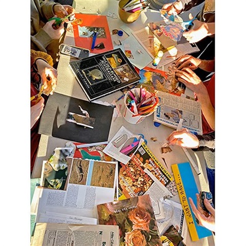 People sitting around a big table covered in newspapers, magazines and craft supplies.