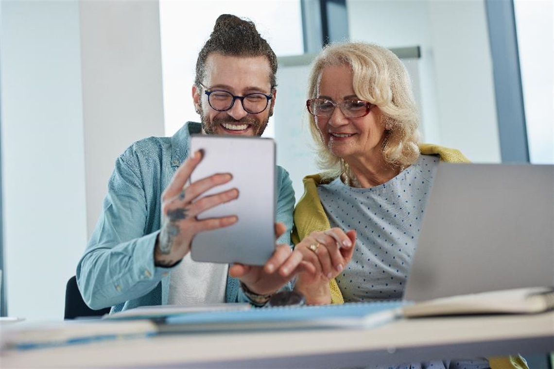 A man and woman using a tablet and a laptop.