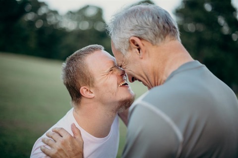 A person with down syndrome and his father in a loving embrace. 