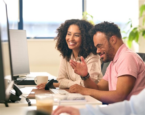 Two people work together on a desktop computer.