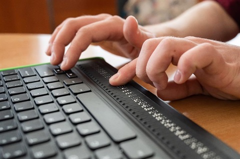A man types at a keyboard with a Braille display.
