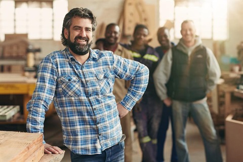 A man leans against a wooden bench in a workshop.