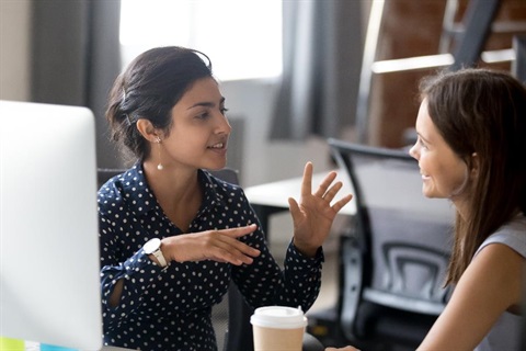 Two women talking over coffee and a work desk.
