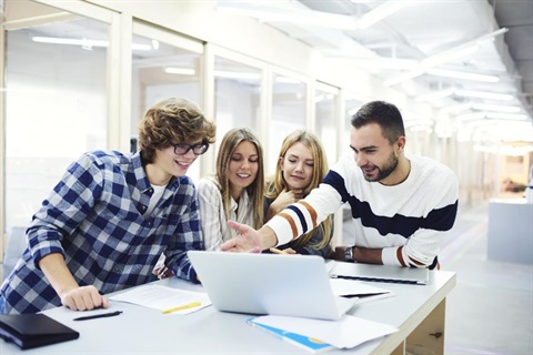 a man and three youths gather around a table with a laptop on it. 