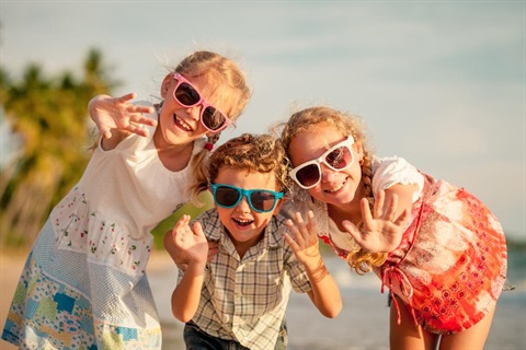 Three children smiling and waving. 