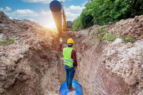 A worker directs a crane placing a large pipe in the ground.