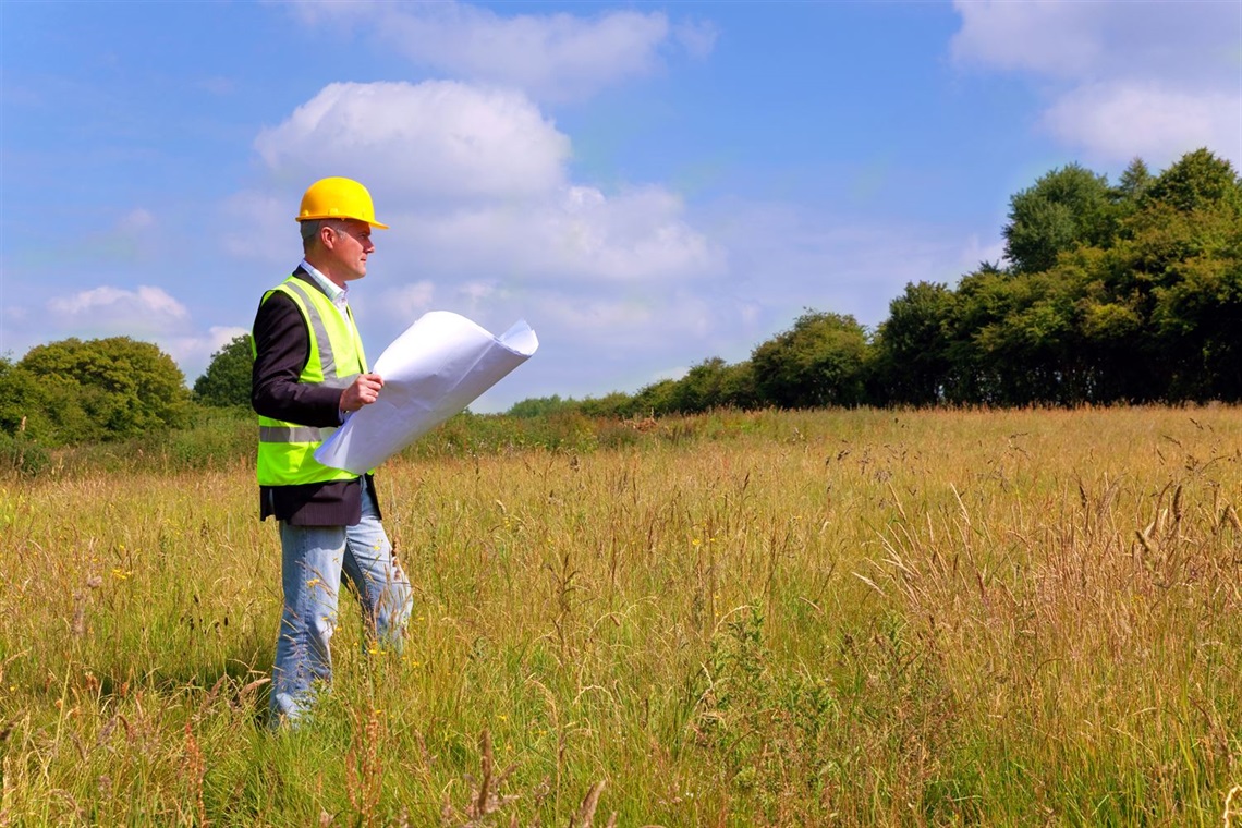 stock image of a man looking at building blueprints in a field