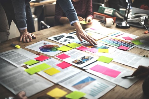 People gathered around a table that is covered in print outs and colourful sticky notes.