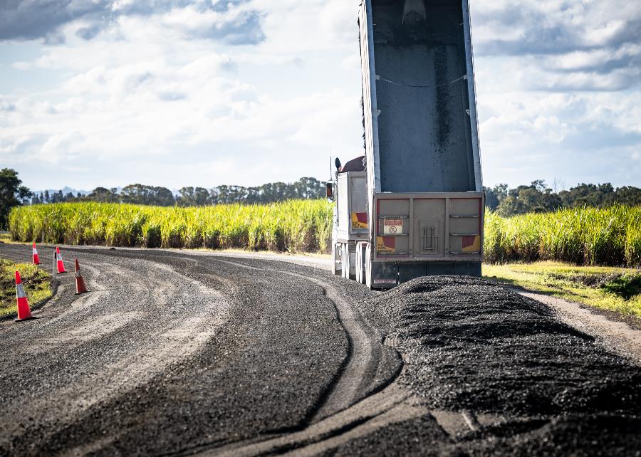 A B-double truck dumps gravel on to a road that is being upgraded.