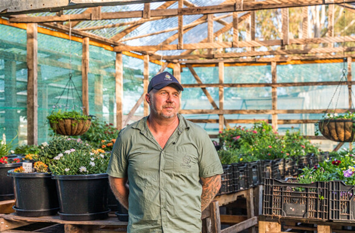 a man stands in front of plants in a greenhouse